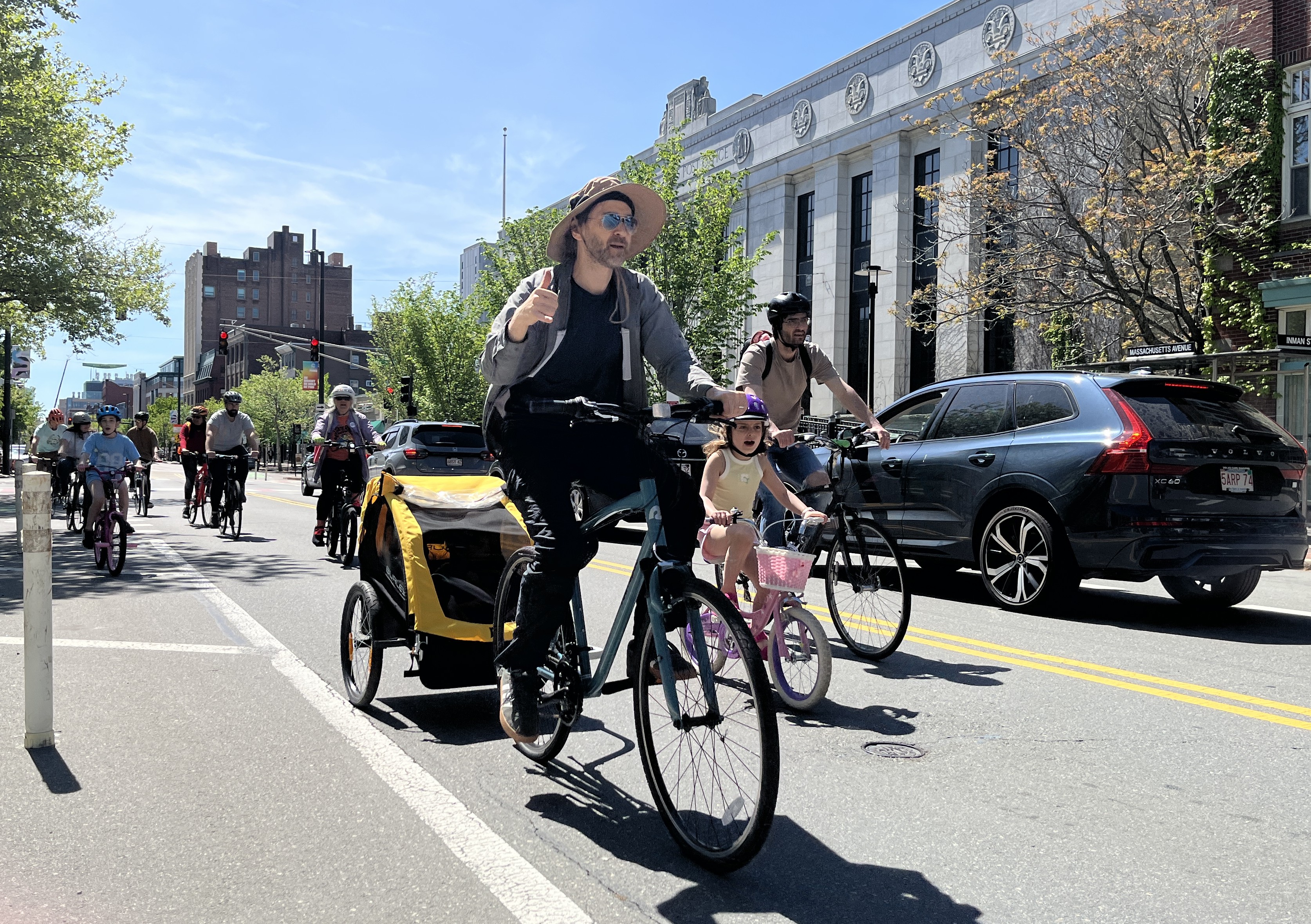 A person rides a bike with a trailer attached and a child inside.