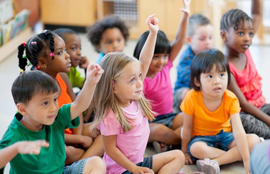 a classroom of preschoolers raise their hand