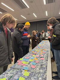 A group of about six people gather around a map with sticky notes.