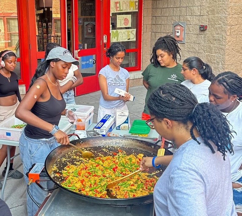 A group of young people cooking paella in a large pot outside Moses Youth Center in an activity with PAGU restaurant