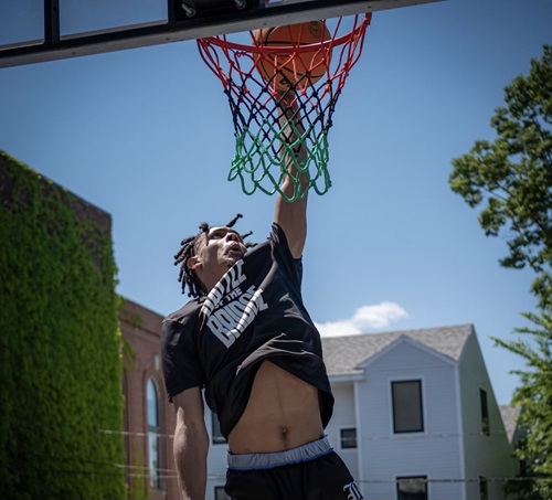 A basketball player dunks on a basketball hoop displaying a Juneteenth-inspired net with red, black, and green colors 