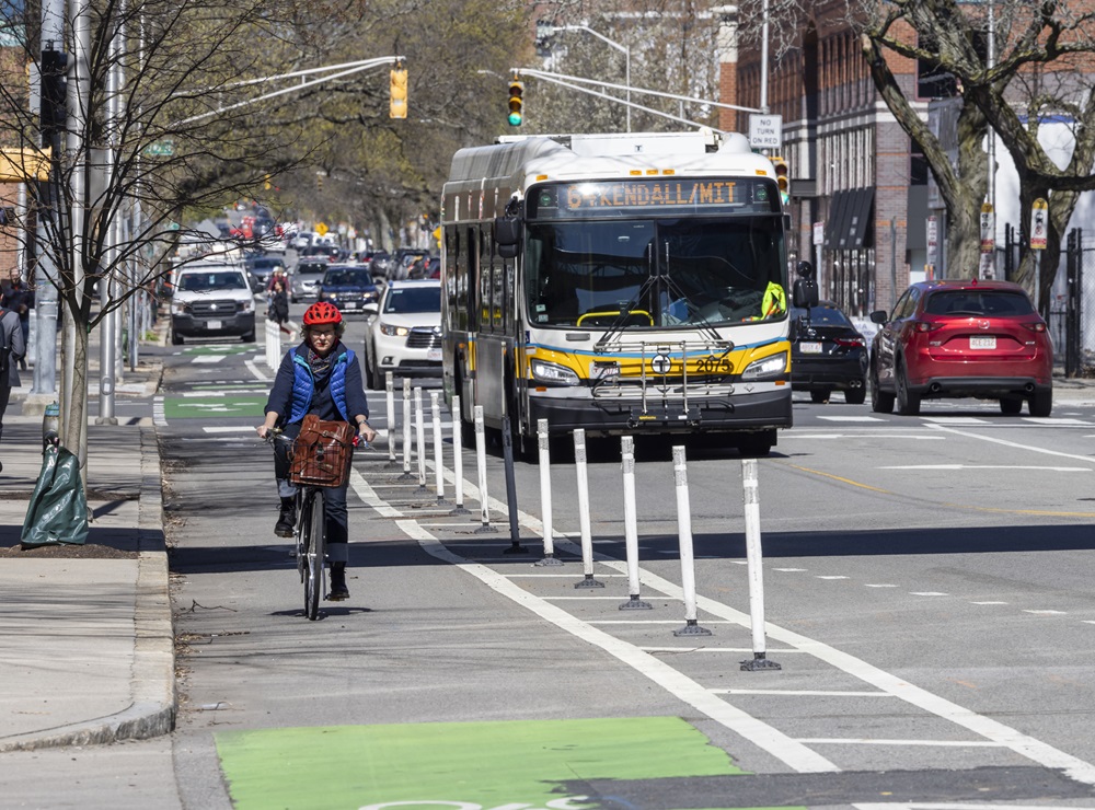 A Cambridge cyclist bikes along a separated bike lane while a bus trails behind