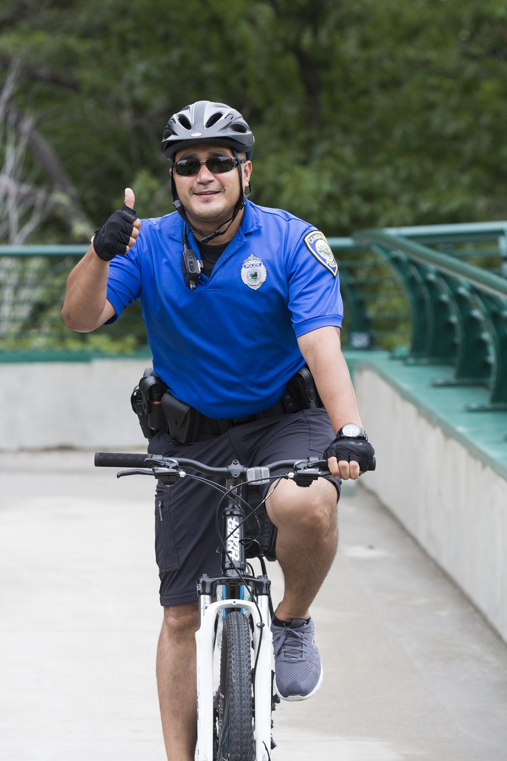 A Cambridge Police officer rides a bike while giving the camera a thumbs up