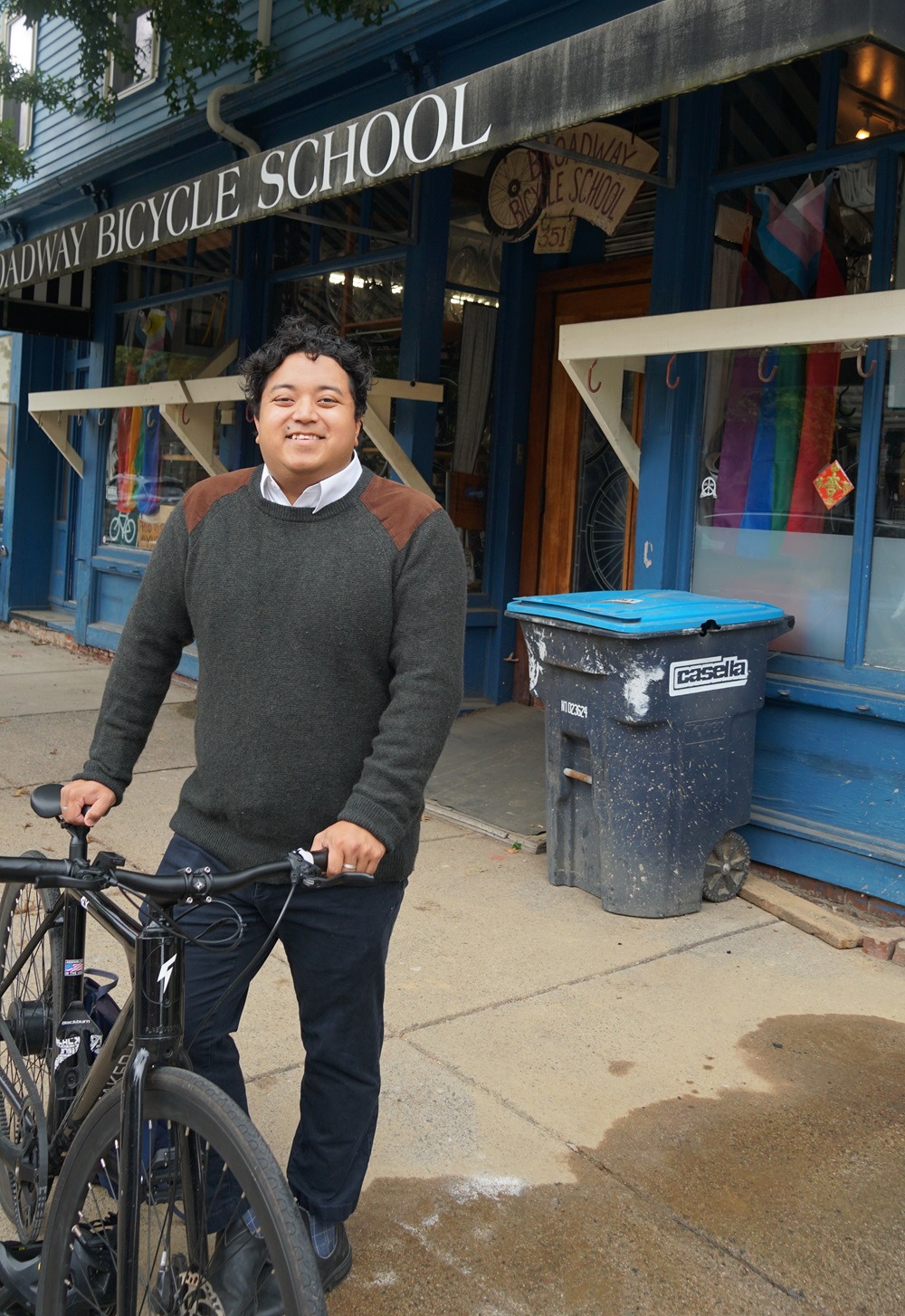 Active Transportation Coordinator for the Community Development Department, Tenzin Choephel, stands with a Bluebike in front of Broadway Bicycle School.