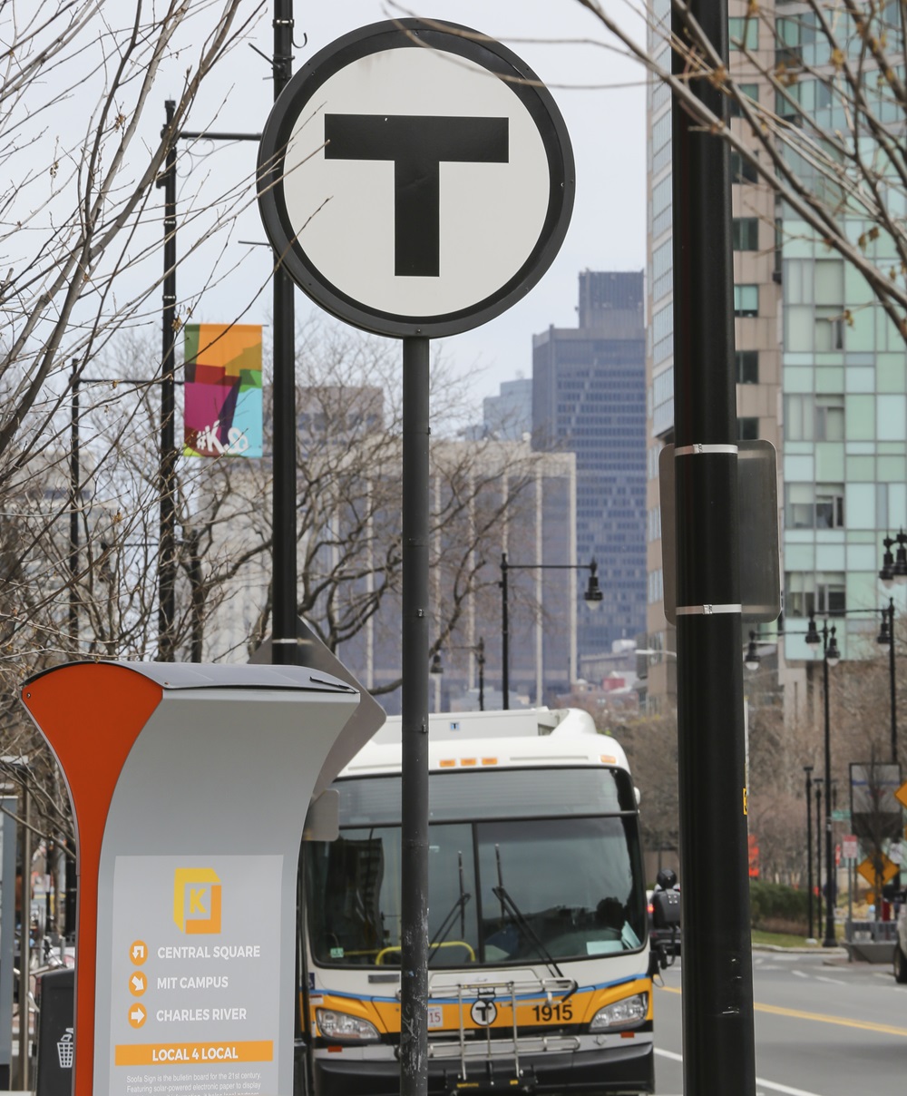 An MBTA bus is parked in front of a T stop in Kendall Square.