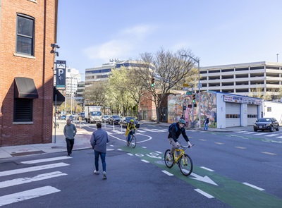 Pedestrian and two cyclist crossing intersection, mural in the background