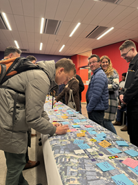 people standing around a map on the table with sticky notes. some people writing on sticky notes