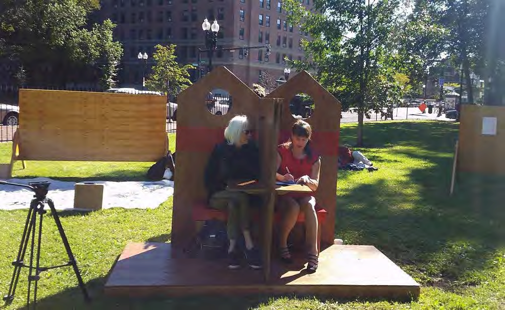 Two people sitting on a bench talking through a partition between them