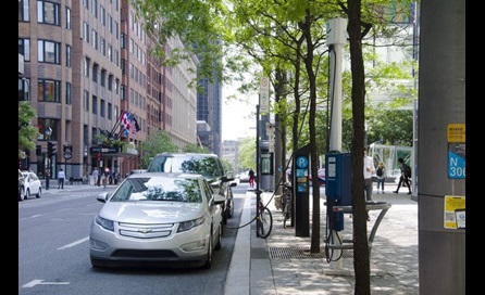 An electric vehicle parked on a City street plugged into a curbside charger