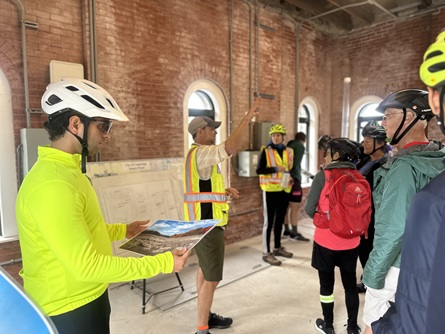 People stand in the winter street gatehouse at Hobbs Brook Reservoir. The walls are red brick, and there is a poster map of the watershed.