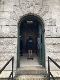 A person stands framed by a doorway. The building is granite, with an arched, green painted door.