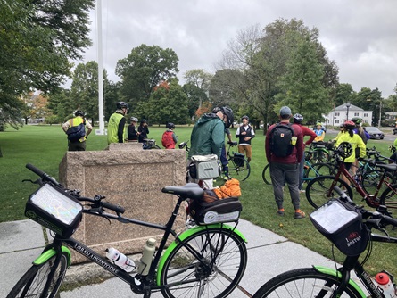 Bikes lean against a platform at Lexington Battle green. In the background are riders and guides during a history talk.