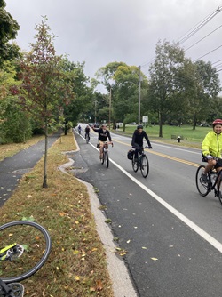 People smile and wave at the camera while biking along a road.