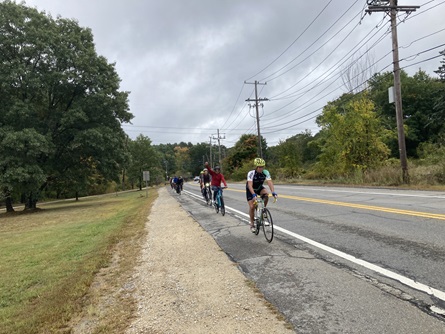 People smile and wave at the camera while biking along a road.