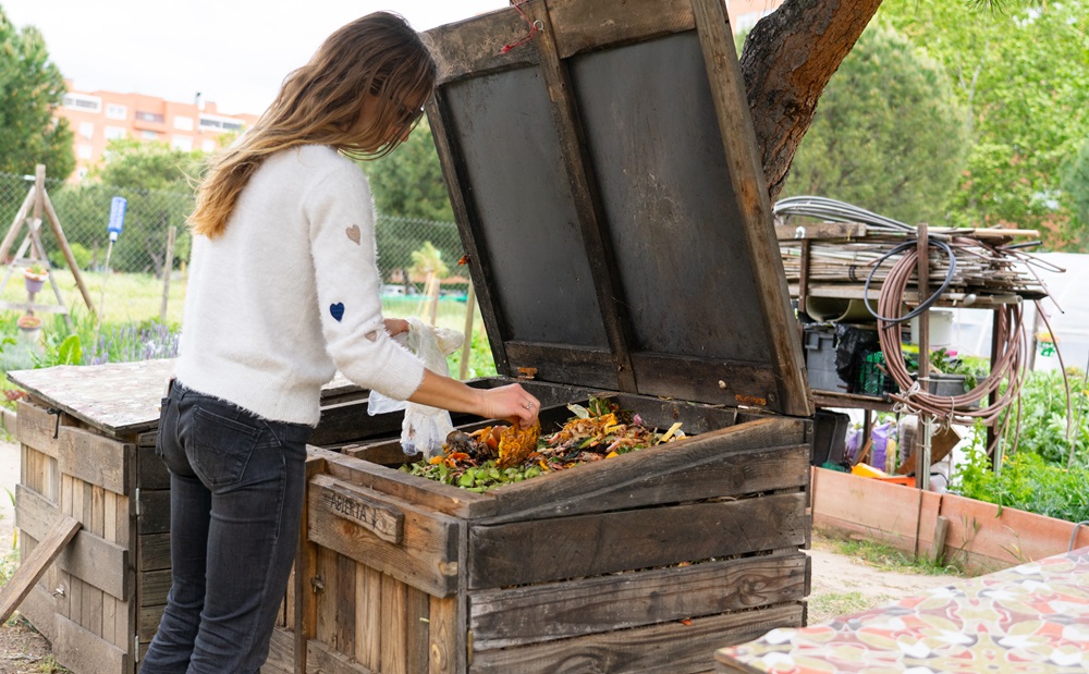 Person composting kitchen waste in a large wooden bin at a community garden.