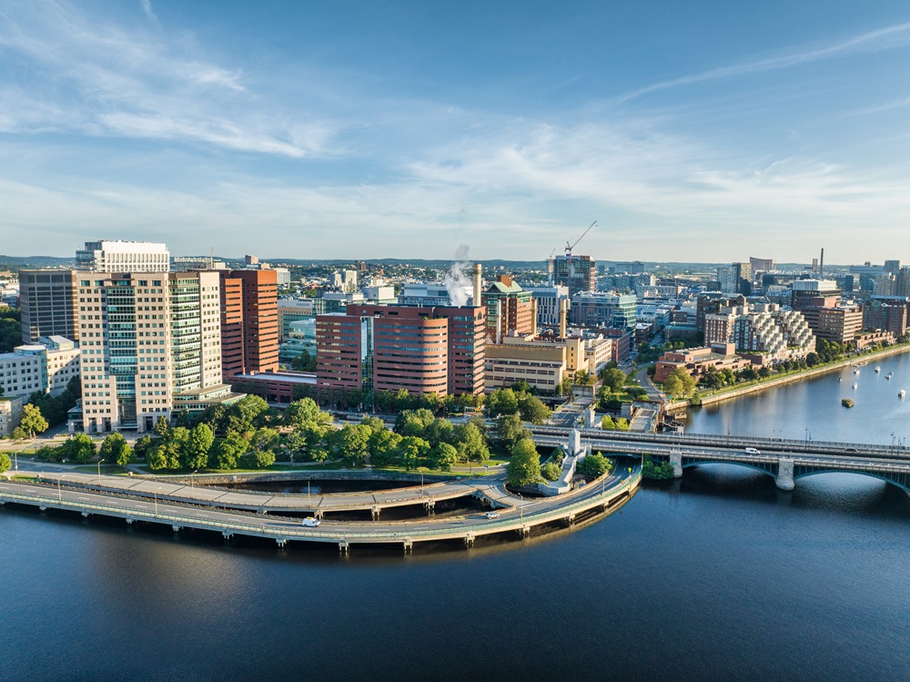 Aerial view of the Charles River and the Massachusetts Institute of Technology campus in Cambridge, Massachusetts, featuring modern buildings and a bridge connecting over the river.